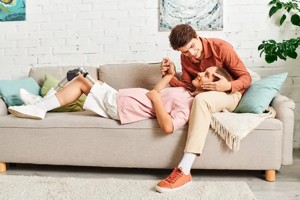 A woman with a prosthetic leg rests on the couch while her boyfriend smiles at her. — Stock Photo