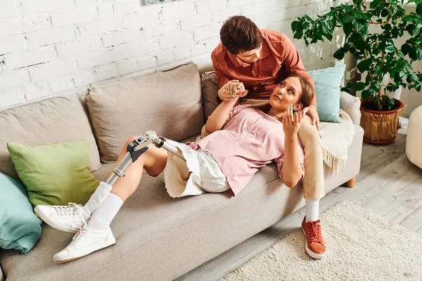 Une femme avec une jambe prothétique repose sur un canapé tandis que son petit ami est assis à côté d'elle. — Photo de stock