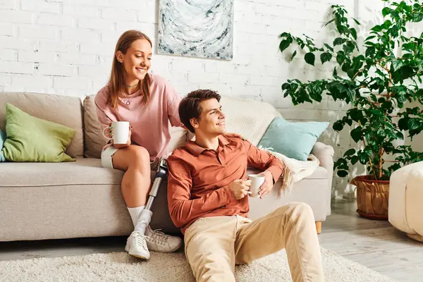 A woman with a prosthetic leg sits on a couch with her boyfriend, enjoying a cup of coffee together. — Stock Photo