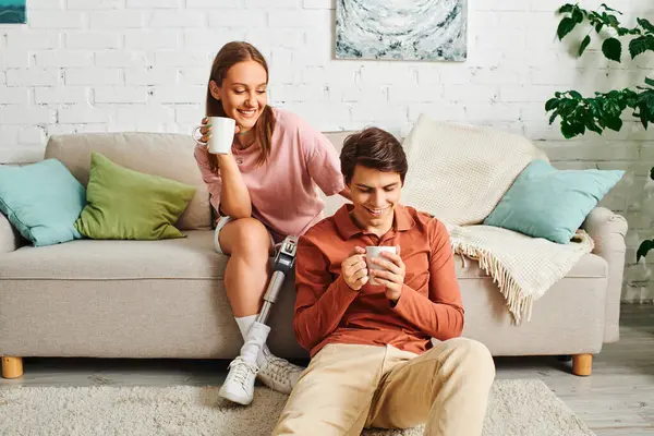 A woman with a prosthetic leg and her boyfriend enjoy a cup of coffee together on a couch. — Stock Photo