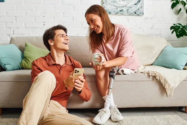 Young couple chilling at home: woman on sofa with cup, man on floor on phone. — Stock Photo