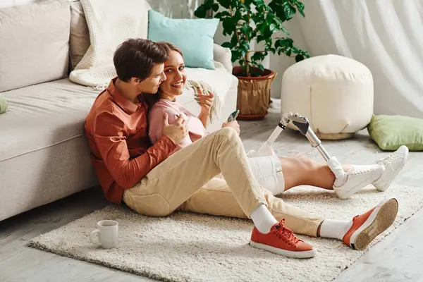 A woman with a prosthetic leg embraces her boyfriend while sitting on a rug in a living room. — Stock Photo