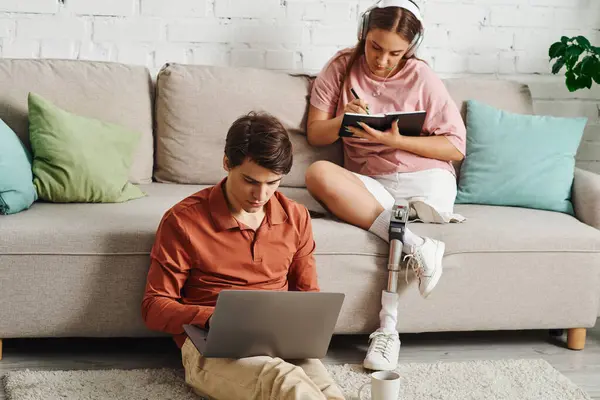 A woman with a prosthetic leg sits on a couch while her boyfriend works on a laptop. — Stock Photo