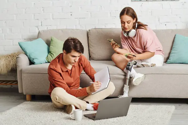 Woman with prosthetic leg texts on couch while boyfriend works nearby. — Stock Photo