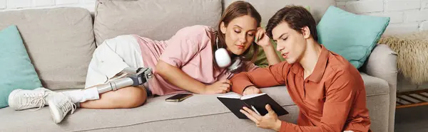 A woman with a prosthetic leg and her boyfriend relax on a couch, sharing a book together. — Stock Photo