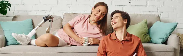 A woman with a prosthetic leg smiles and laughs with her boyfriend on a comfortable sofa. — Stock Photo