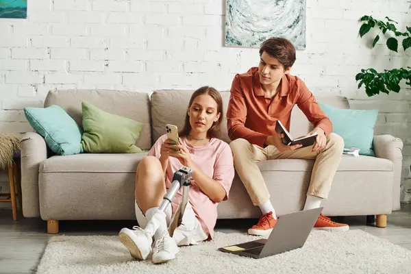 A young woman with a prosthetic leg sits on the floor while her boyfriend relaxes on the couch. — Stock Photo