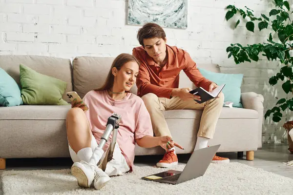A woman with a prosthetic leg sits on the floor with her boyfriend while looking at a laptop. — Stock Photo
