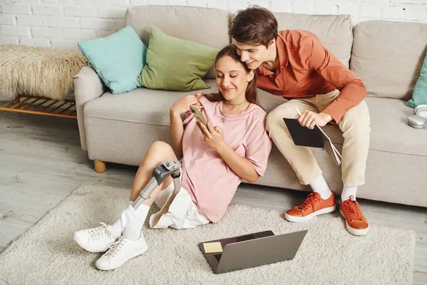 A woman with a prosthetic leg sits on the floor while her boyfriend leans against the couch. — Stock Photo