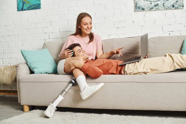 A woman with a prosthetic leg and her boyfriend are relaxing on a sofa, sharing a laugh together. — Stock Photo
