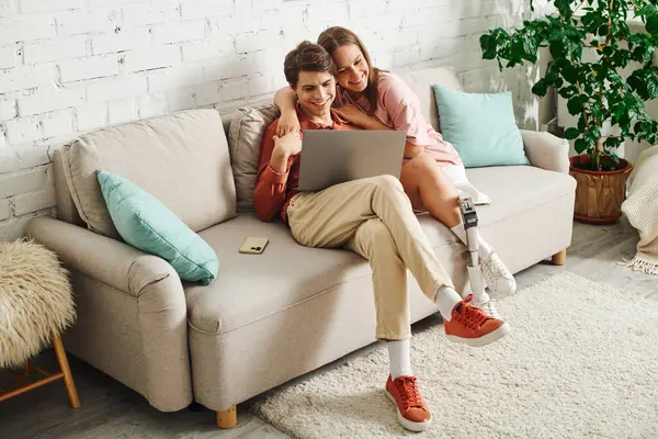 A young couple sitting on a sofa, looking at a laptop together. — Stock Photo