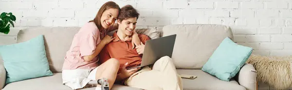 Woman with prosthetic leg cuddles her boyfriend on the couch, watching something on a laptop. — Stock Photo