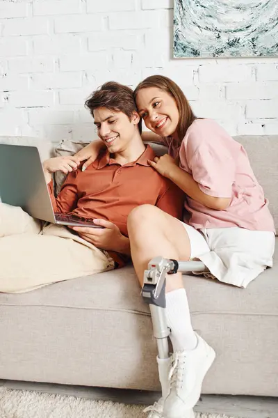 A woman with prosthetic leg cuddling with boyfriend on couch watching laptop. — Stock Photo
