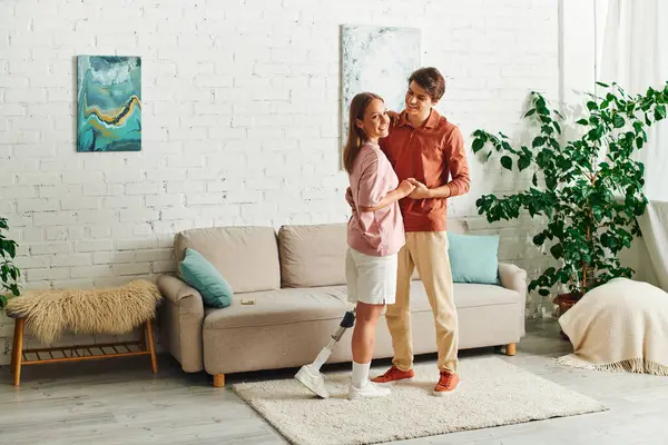 A woman with a prosthetic leg dances with her boyfriend in their cozy living room. — Stock Photo