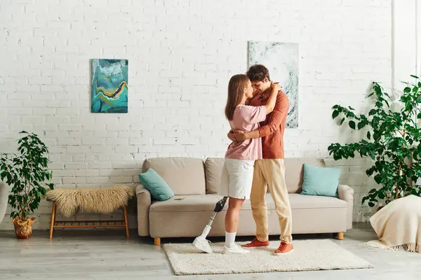 A woman with a prosthetic leg embraces her boyfriend in their living room. — Stock Photo