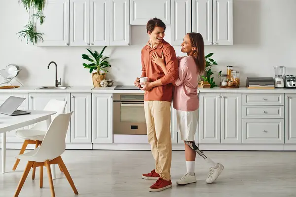 A woman with a prosthetic leg embraces her boyfriend in a modern kitchen. — Stock Photo