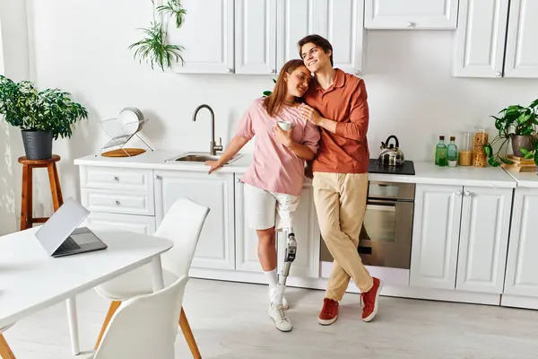 A woman with a prosthetic leg leans against her boyfriend in a modern kitchen. — Stock Photo