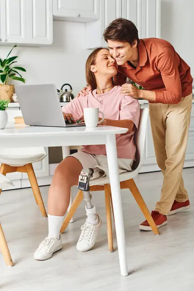 A woman with a prosthetic leg sits at a table with her boyfriend, who is leaning in to kiss her. — Stock Photo