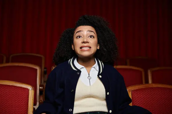 Uma jovem mulher em roupas casuais elegantes senta-se em um cinema, reagindo com surpresa e olhos largos para a tela. — Fotografia de Stock