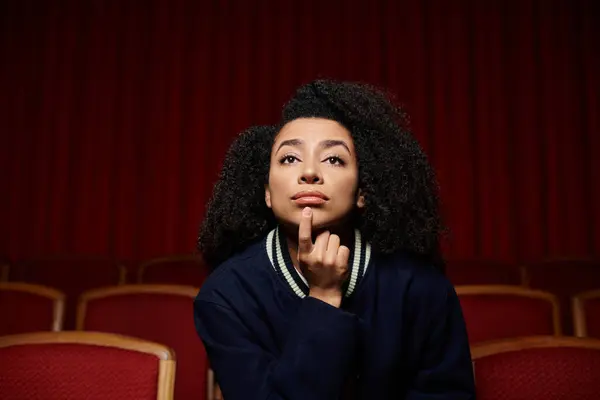 A young woman in stylish casual clothes watches a movie in a cinema, her expression a mixture of awe and contemplation. — Stock Photo