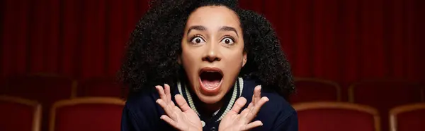 A young woman watches a movie in a theater, her face filled with surprise and excitement. — Stock Photo