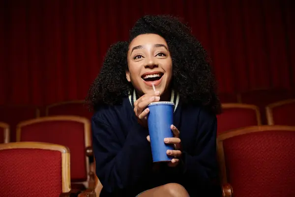 Una giovane donna siede su un sedile di un cinema, sorridente e ridente mentre guarda un film. — Foto stock