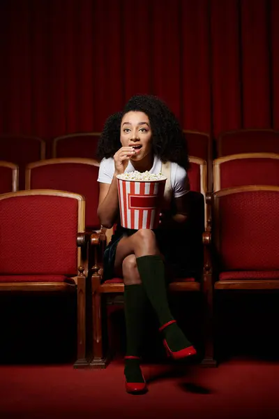 A young woman, engrossed in the movie, enjoys a bucket of popcorn. — Stock Photo