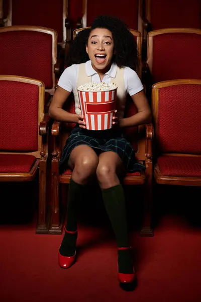 Una giovane donna in elegante abbigliamento casual siede in un sedile del teatro con un secchio di popcorn — Foto stock
