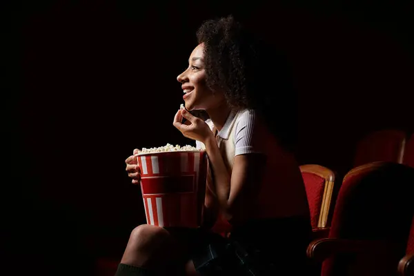 A young woman enjoys a movie while munching on popcorn in a dark theater. — Stock Photo