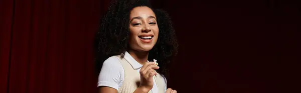 A young African American woman in stylish casual clothes watches a movie in a cinema, her expression revealing her enjoyment. — Stock Photo