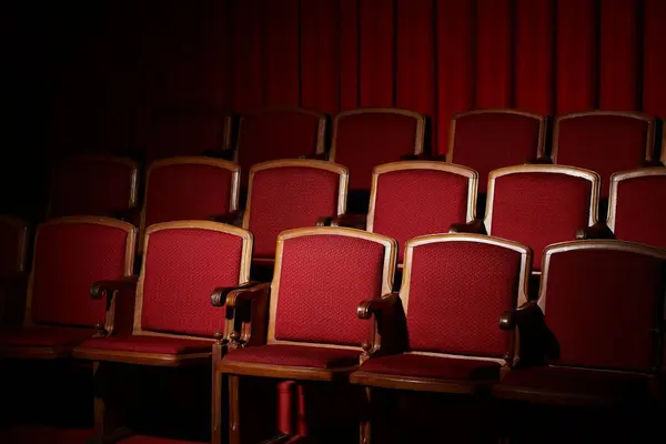 Fileiras de assentos de veludo vermelho vazios em um cinema escurecido, antecipação paira no ar. — Fotografia de Stock