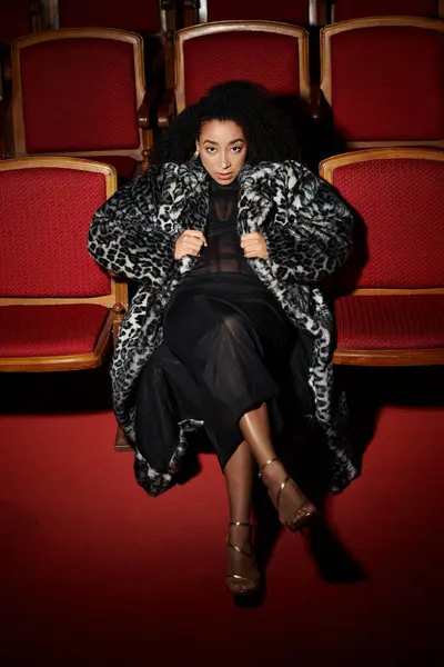 A stylish woman in a leopard-print coat sits in a theater, reacting to the film. — Stock Photo