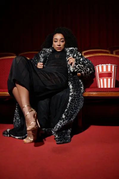 Une femme élégante en manteau imprimé léopard regarde un film dans un cinéma, captivée par le film. — Photo de stock