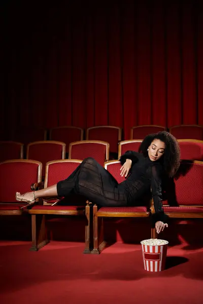 An elegant African American woman in black watches a movie in a theater, captivated by the film. — Stock Photo