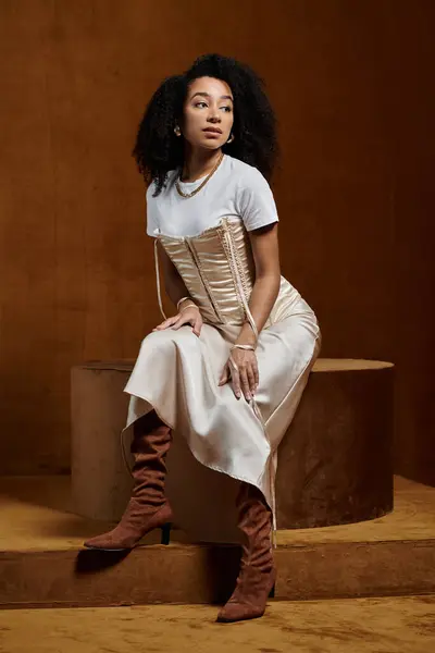 Una mujer afroamericana con estilo posa en un ambiente de estudio, vistiendo una parte superior blanca, un corsé de color crema y una falda que fluye. - foto de stock