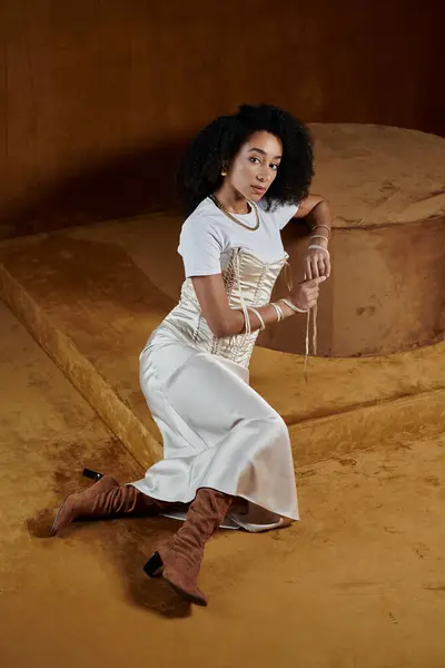 A stylish African American woman in a white outfit poses in a studio setting with a warm, earthy backdrop. — Stock Photo