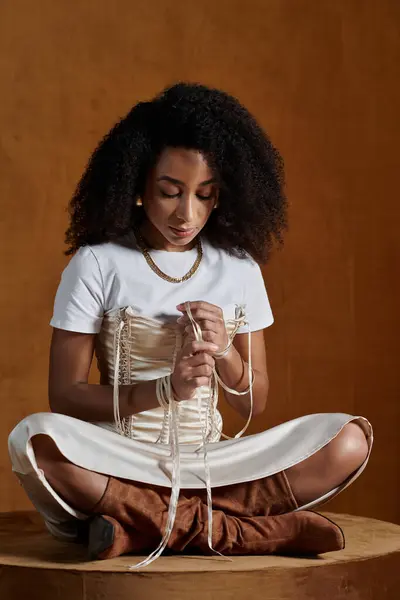 A stylish African American woman sits in a studio, her fingers gently adjusting the straps of her trendy outfit. — Stock Photo