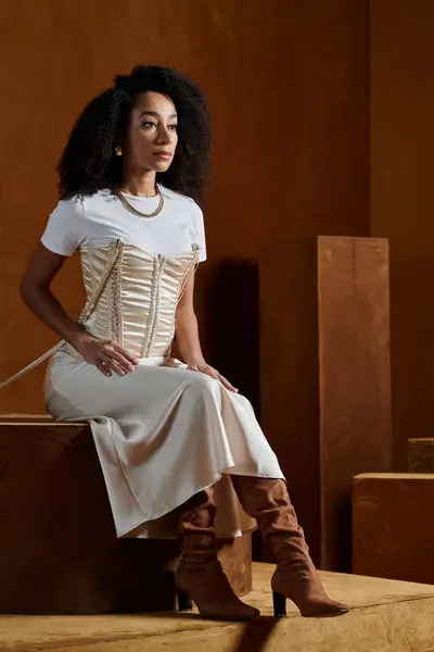 A stylish African American woman poses in a trendy outfit while sitting on a wooden platform. — Stock Photo