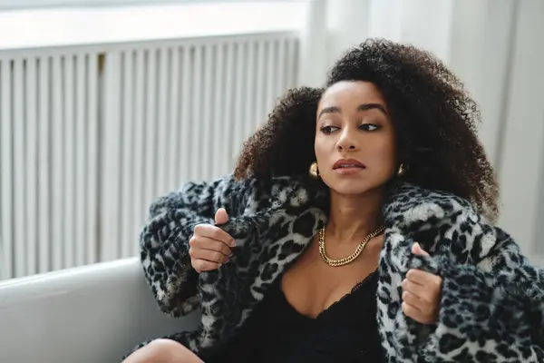 A young woman with curly hair poses in a studio wearing a leopard print coat and black top. — Stock Photo