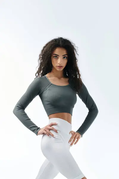 A young Black woman with long curly hair poses in a green crop top and white leggings. — Stock Photo