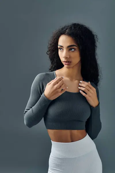 Una giovane donna afroamericana in abito da allenamento si erge su uno sfondo grigio, guardando da un lato. — Foto stock