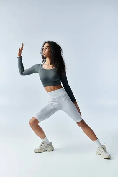 A young, beautiful Black woman in white shorts stretches her leg, reaching towards the sky, with a determined look on her face. — Stock Photo