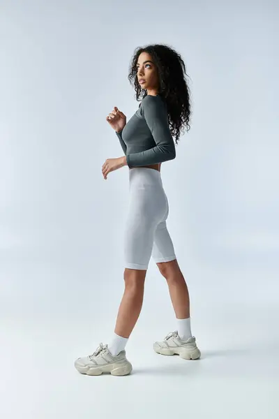 Eine junge Frau schreitet selbstbewusst über eine weiße Kulisse und demonstriert Stärke und Athletik. — Stockfoto