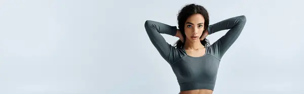 A young African American woman in a grey top stretches with her arms behind her head, looking at the camera. — Stock Photo