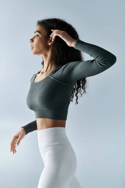 A young woman wearing a long-sleeved top and white leggings, stretches and poses in studio — Stock Photo