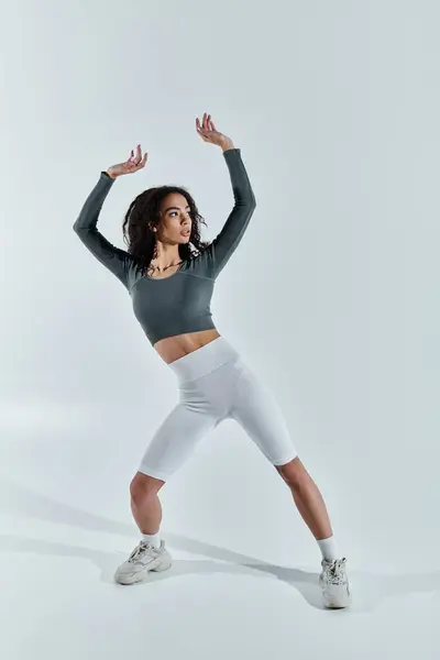 A young Black woman in a green top and white shorts stretches her arms above her head while facing away from the camera. — Stock Photo