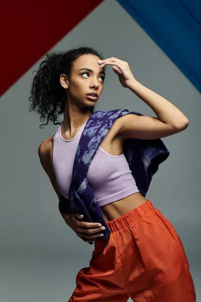 A young woman in athletic wear stretches near a colorful glass panel in a studio with a grey backdrop. — Stock Photo