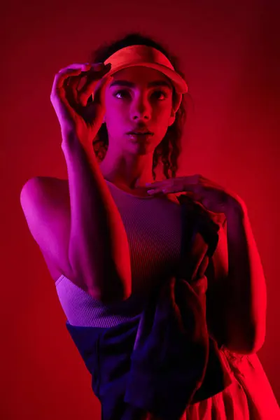 Young African American woman striking a pose in a stylish clothes against a vibrant red backdrop in a neon-lit studio. — Stock Photo