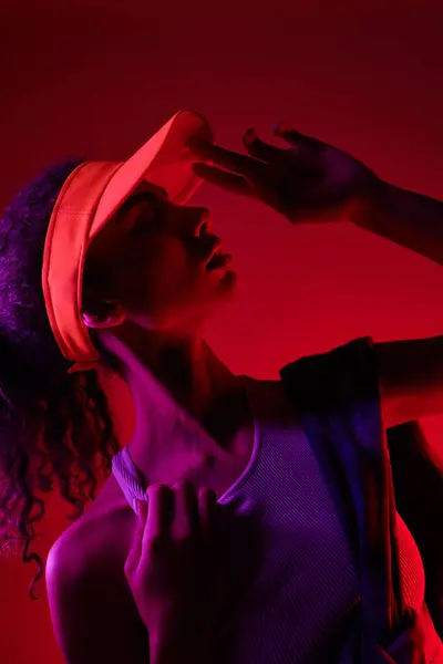 A young woman with curly hair, wearing a visor, poses dramatically in a studio lit by neon lights. — Stock Photo