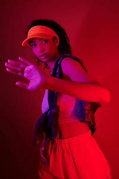 A young woman with dark curly hair and a bright orange visor poses in a studio bathed in neon light. — Stock Photo